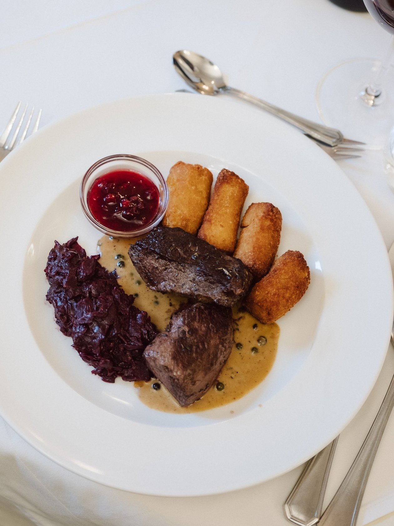 Savor the Taste of Fine Dining Gourmet beef dish presented with croquettes and red cabbage on a plate alongside a small sauce dish