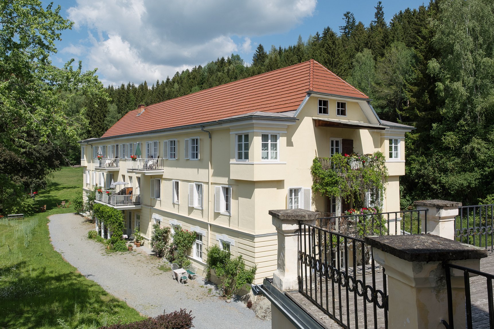 Landsitz Pichlschloss in der Natur Großes, Wohngebäude umgeben von Bäumen und Grünflächen, mit einem Kiesweg davor.