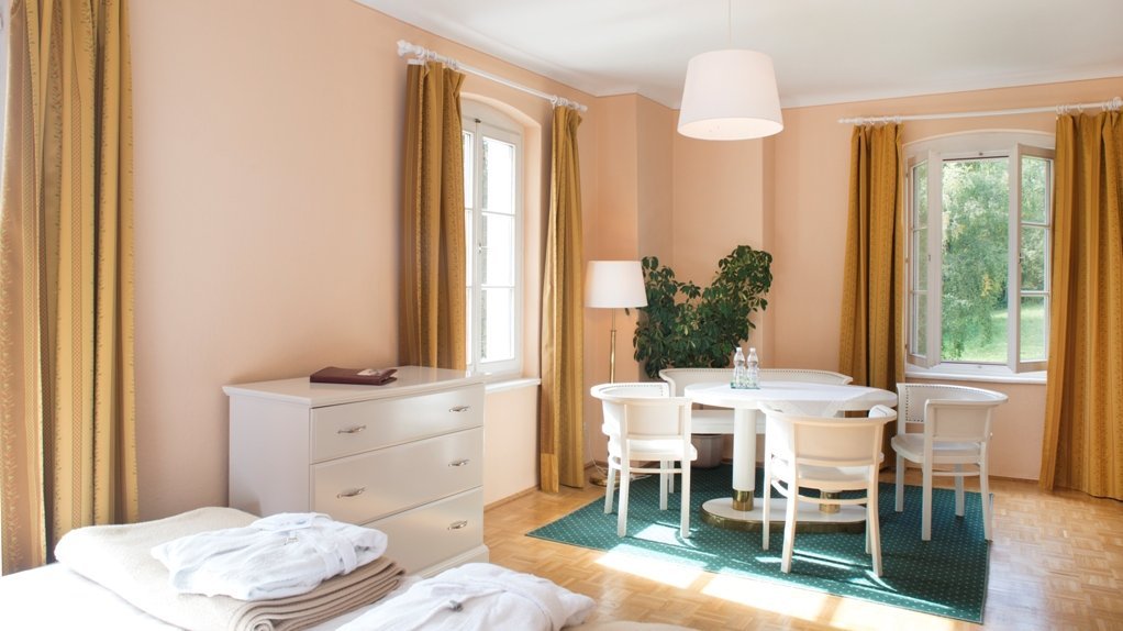 Bright and Inviting Bedroom Retreat A well-lit bedroom featuring peach-colored walls, a dresser, and a small dining area by large windows.
