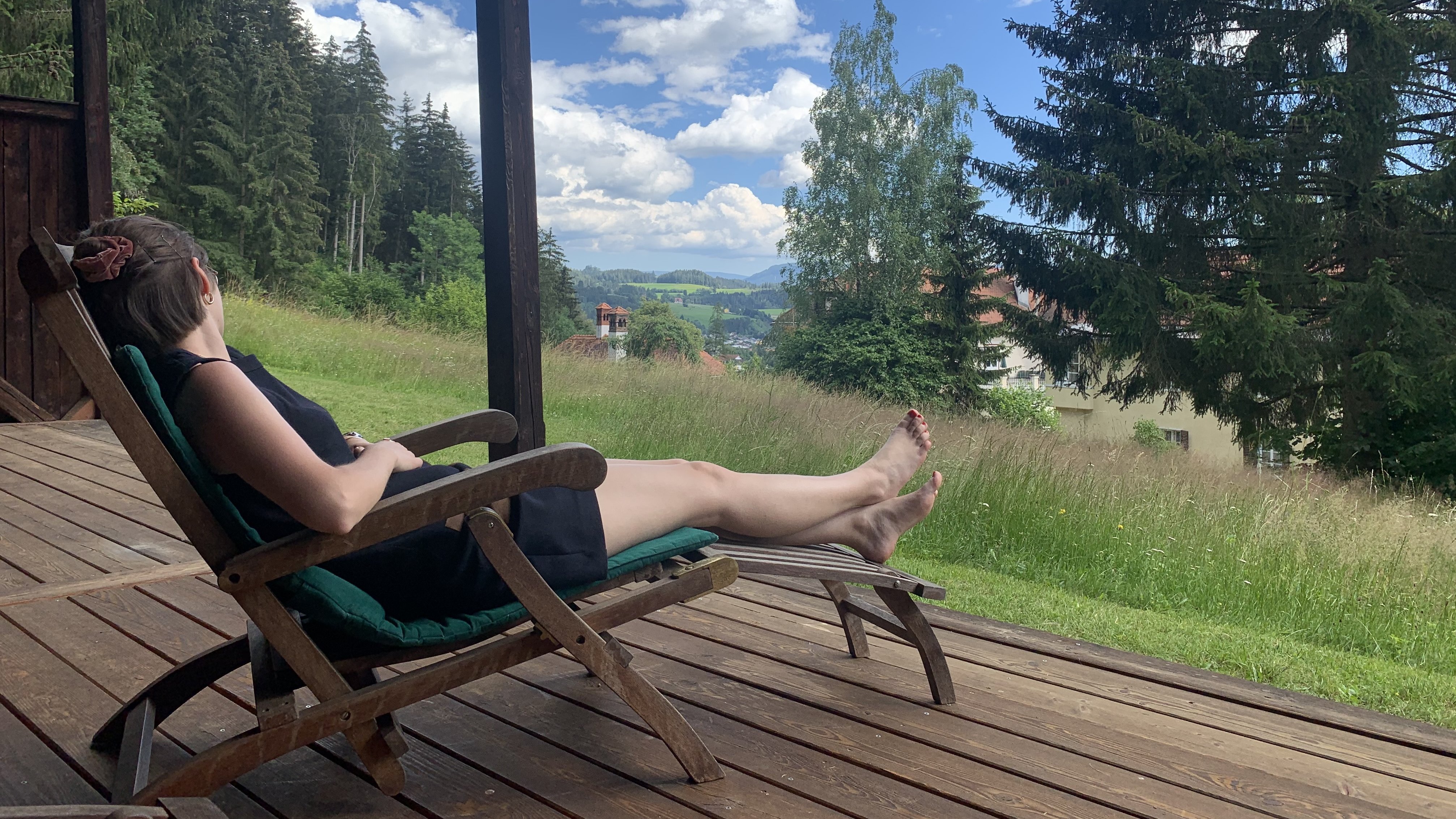 Relax and Unwind in Nature Person reclining on a wooden deck chair with a view of green mountains and clouds