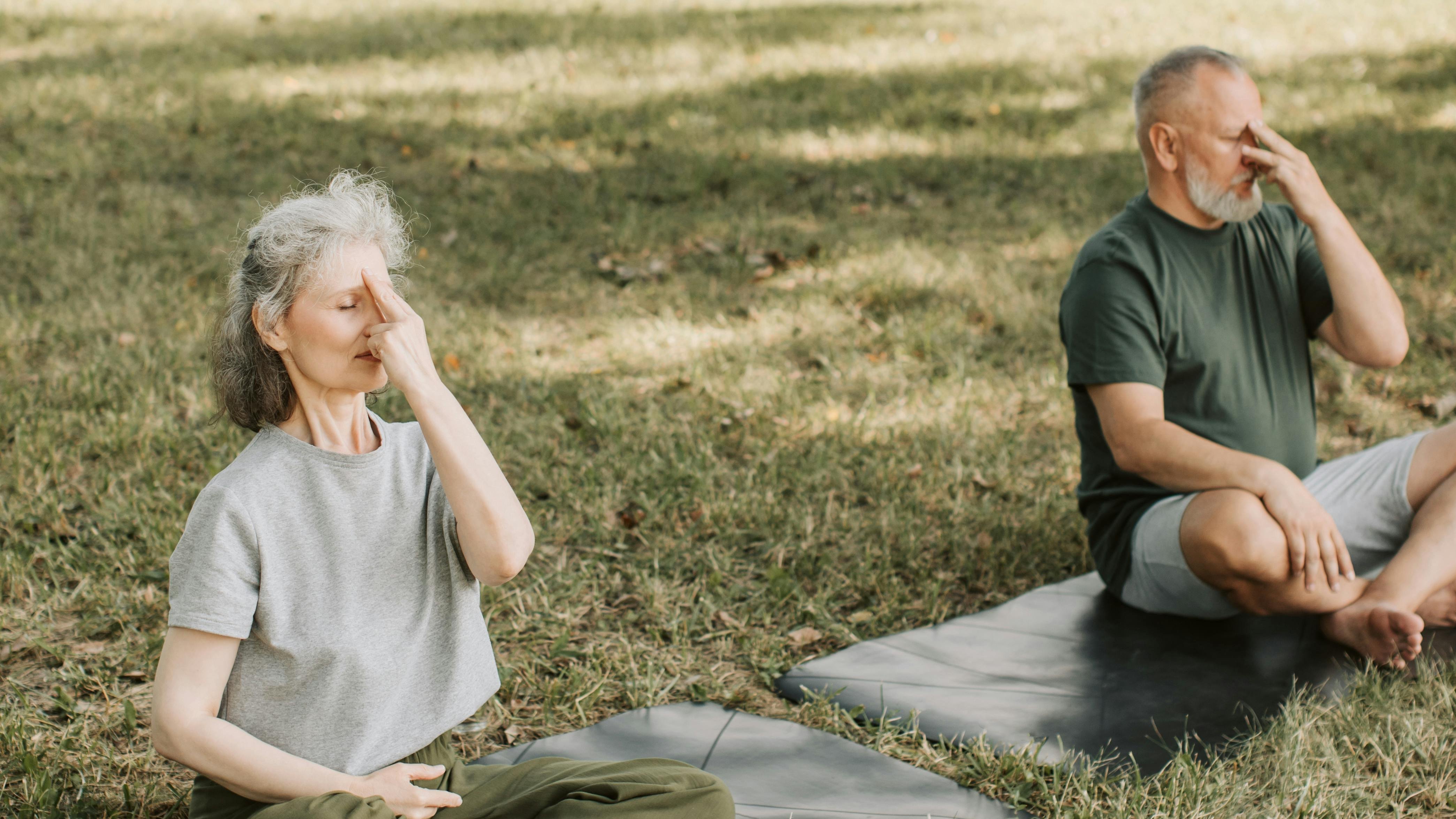 Yoga im Freien für innere Ruhe Zwei ältere Erwachsene praktizieren Yoga im Park auf Yogamatten, konzentriert bei Atemübungen.
