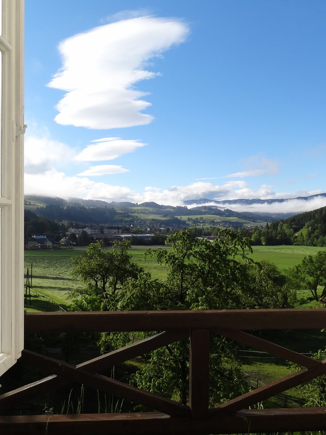 Offenes Fenster mit Bergblick Ein offenes Fenster mit Blick auf eine grüne Landschaft und Berge unter blauem Himmel