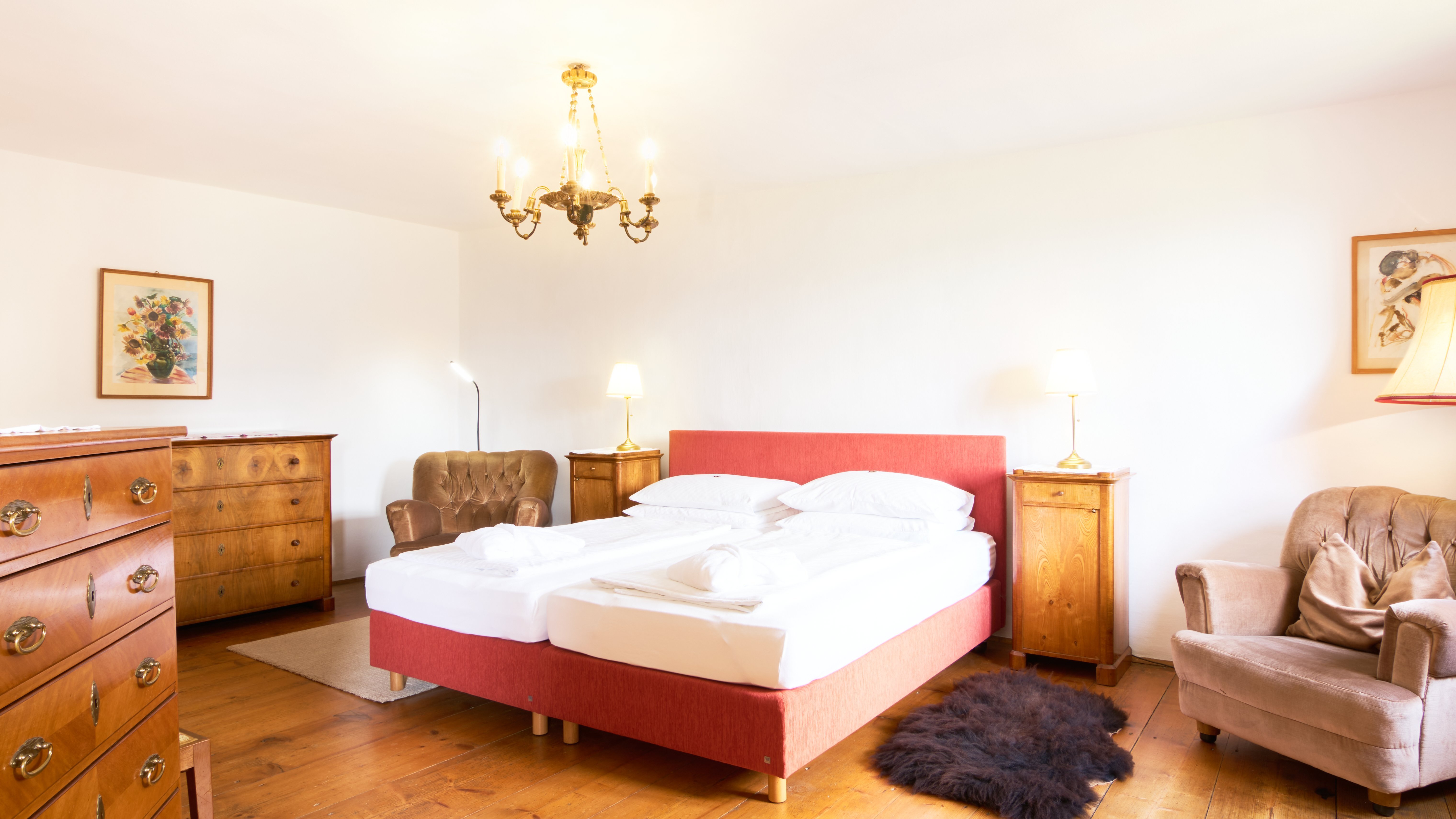 Relax in a beautifully designed bedroom A cozy bedroom featuring a red bed and wooden furniture under warm lighting for comfort