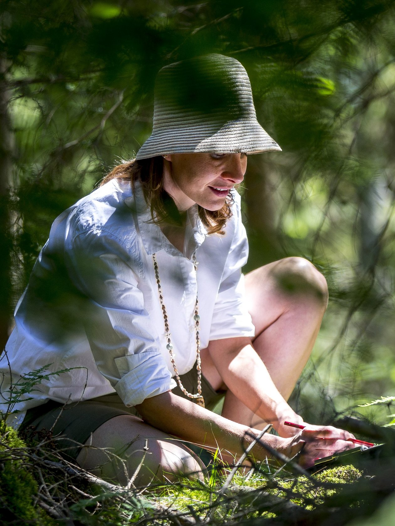 Frau in der Natur Eine Frau sitzt im Wald und genießt die grüne Umgebung bei einer Aktivität im Freien.