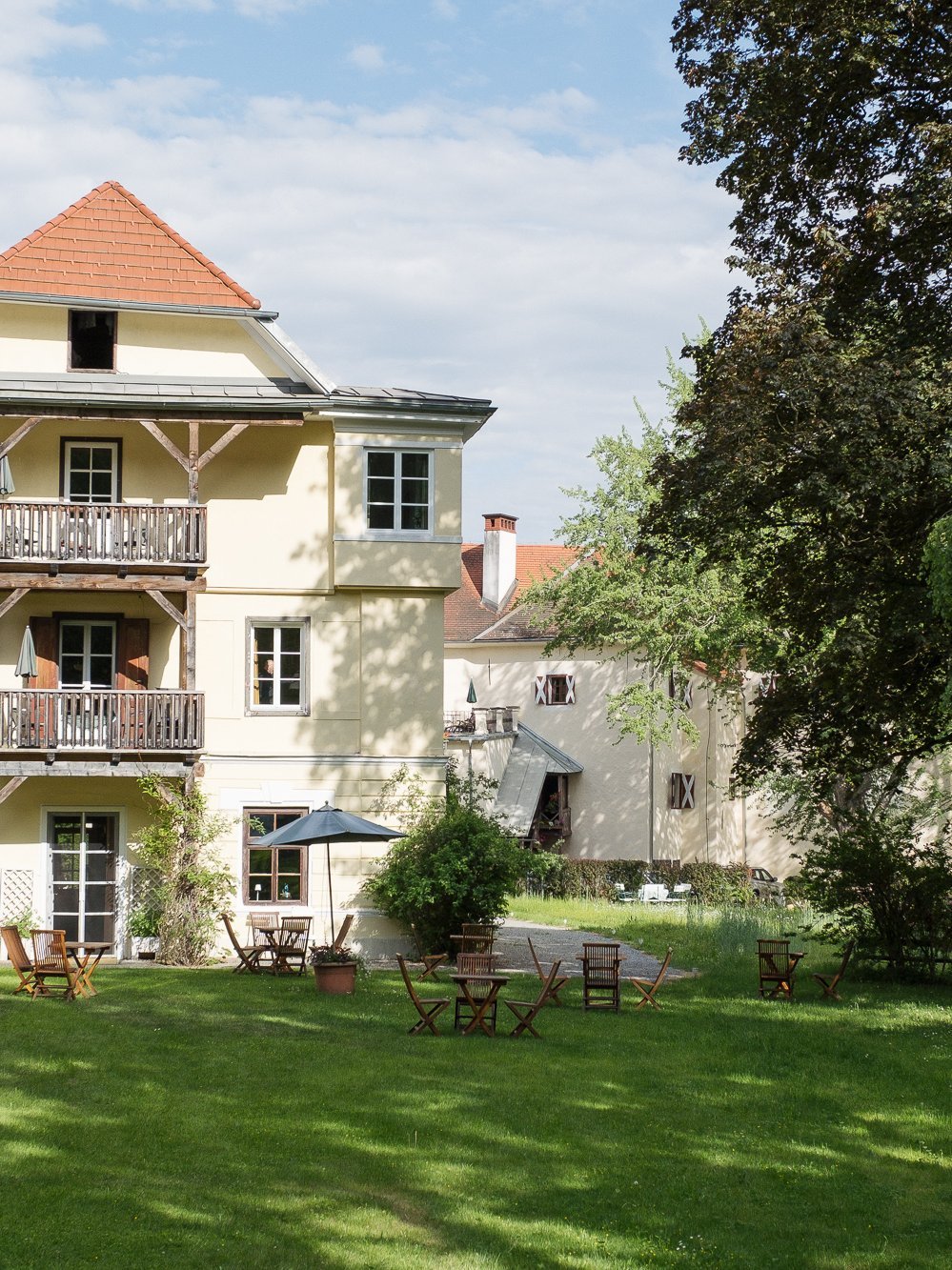 Idyllisches Hotel im Grünen Hotelgebäude mit Sitzgelegenheiten im Freien und Garten umgeben von Bäumen und Grünflächen