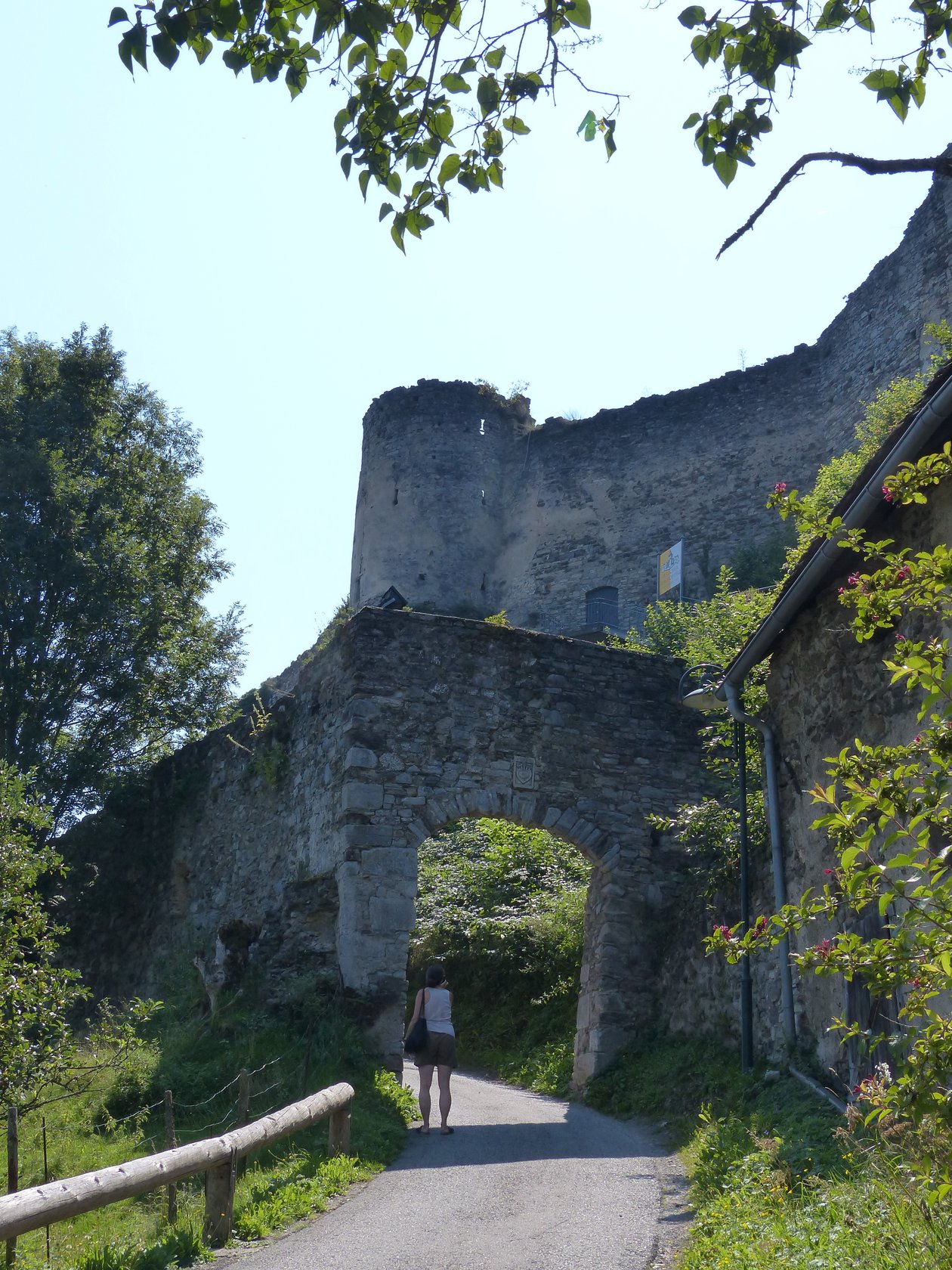 Historische Burgruine im Grünen Person geht einen Weg entlang zu einer Burgruine, umgeben von Bäumen und Grünflächen.
