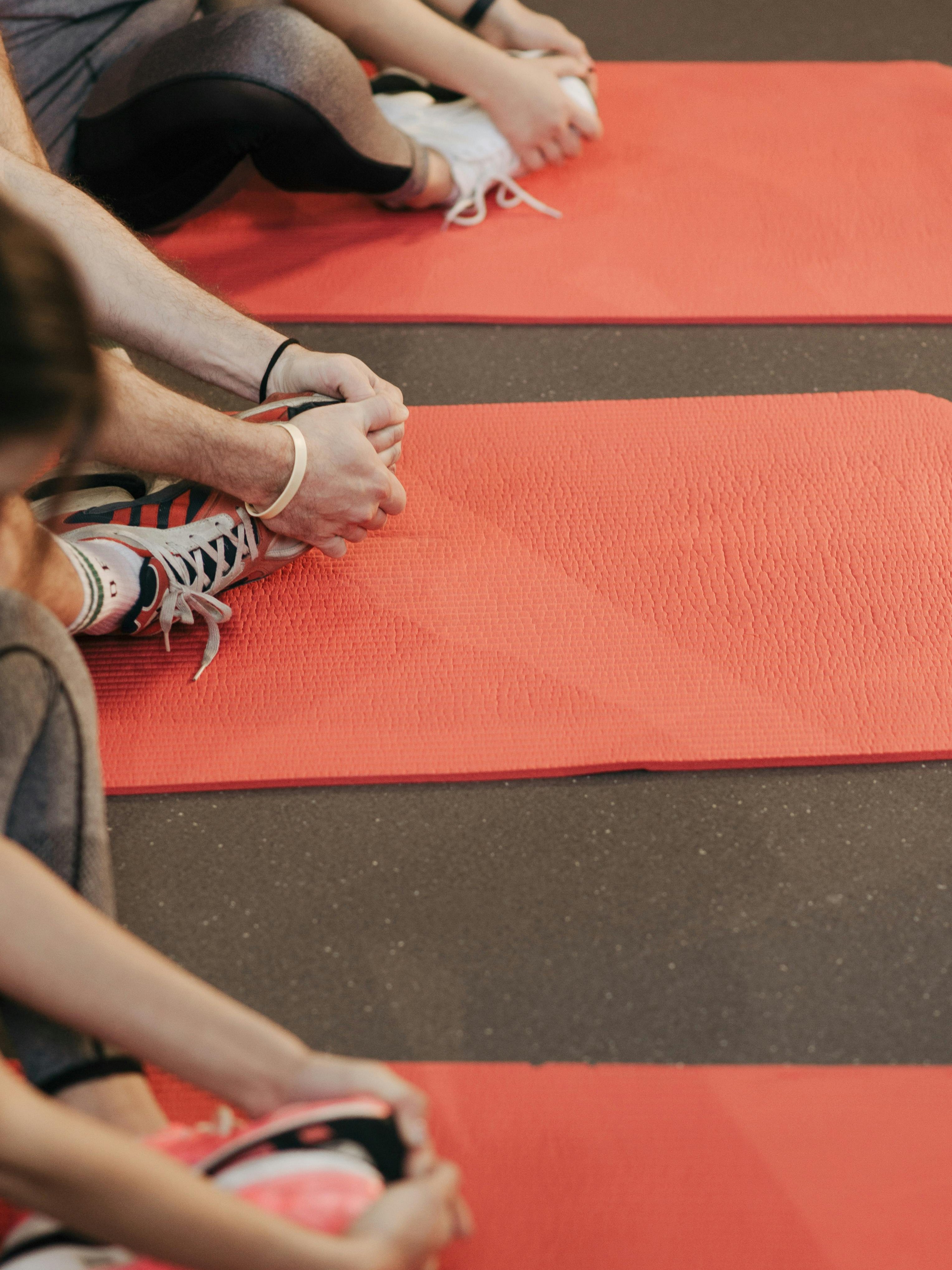 Yoga und Stretching für Wohlbefinden Gruppe von Personen auf roten Yogamatten bei Dehnübungen im Freien, Umgebung wirkt ruhig und entspannend
